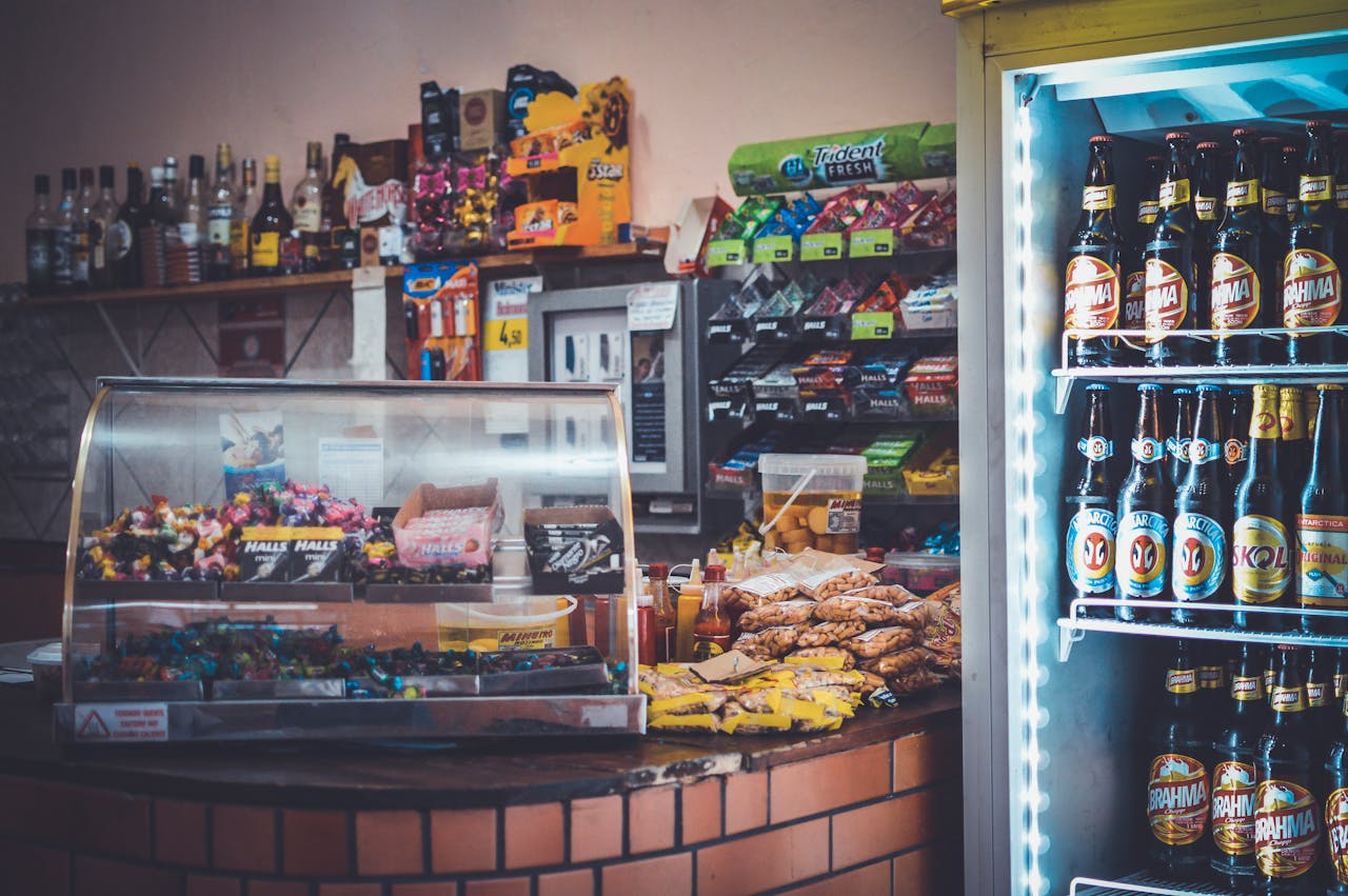 A well-stocked convenience store counter with snacks, drinks, and a refrigerator showcasing beverages.